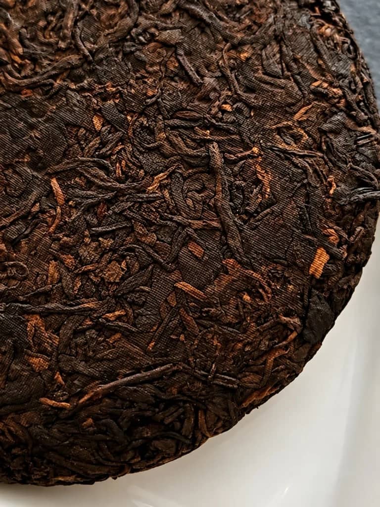 Compressed aged 2010 Jingmai ripe Pu-erh cake showing dark fermented leaves and woven texture