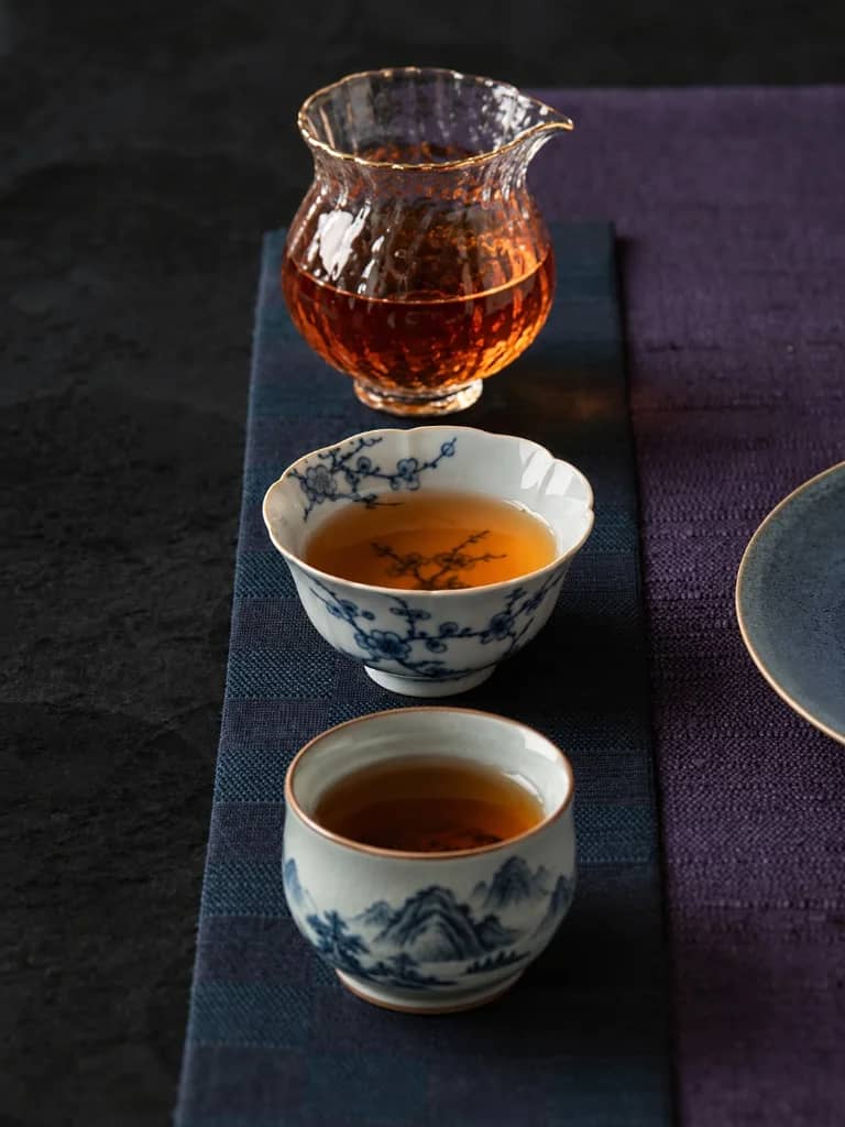 Amber red tea in a ribbed glass pitcher and porcelain tasting cups