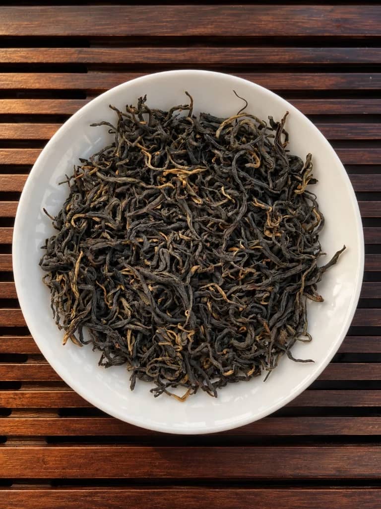 Sun-dried whole Yunnan Shai Hong black tea leaves in a porcelain dish