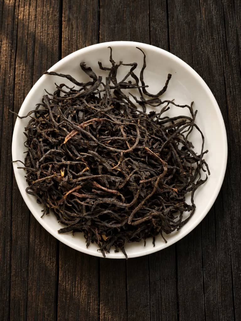 Slender twisted dark wild red tea leaves in a white porcelain dish